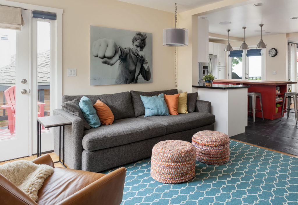 Contemporary colorful living room with gray couch, teal trellis rug, ottomans, and bold art